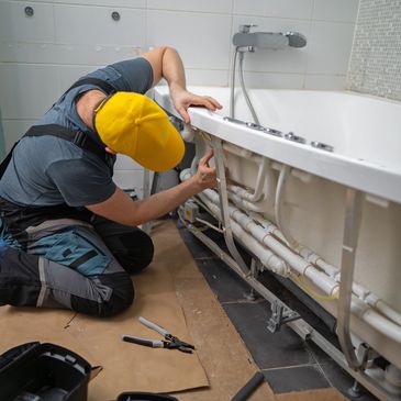 Plumber fixing pipes under a bathtub in a bathroom.