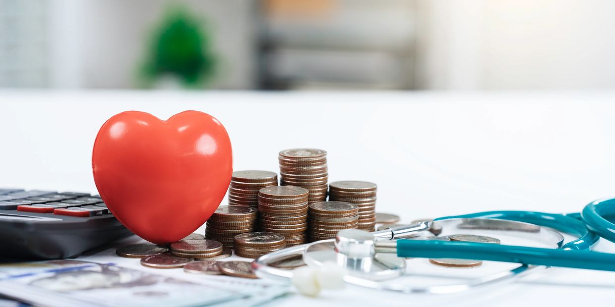 Heart, coins, calculator, and stethoscope on a table.