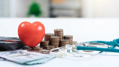 Red heart, coins, and stethoscope on white table.