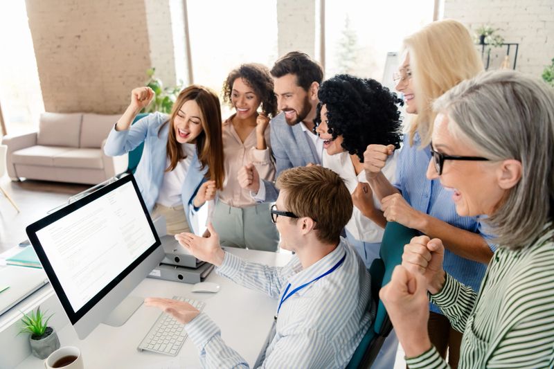 Diverse business team cheers with excitement and teamwork in a contemporary office setting, highlighting collaboration, achievement, and professional dynamics.