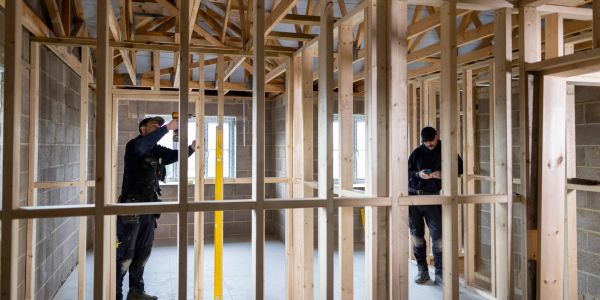 Two workers framing a house interior with wooden beams.