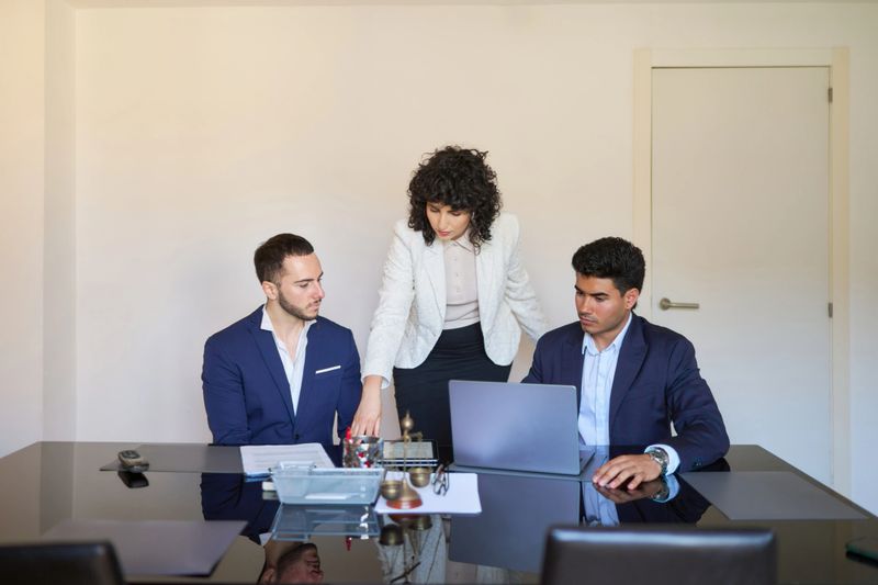 Three lawyers are discussing a case in their office, using a laptop and reviewing documents