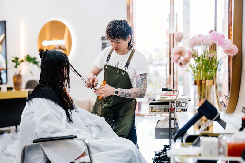 Asian male professional barber cutting woman's hair in hair salon.
