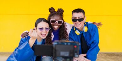 Three friends taking a selfie against a yellow wall.