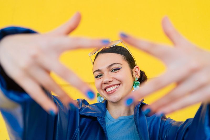 Portrait of a cheerful young woman framing her face with her hands against a vibrant yellow background