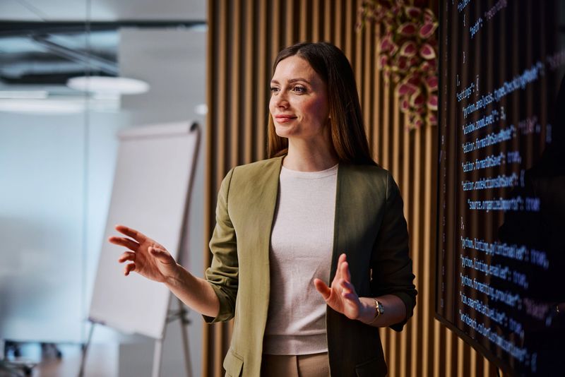 Young adult businesswoman gesturing while presenting a software project using a digital screen, showcasing innovation and technology in the workplace