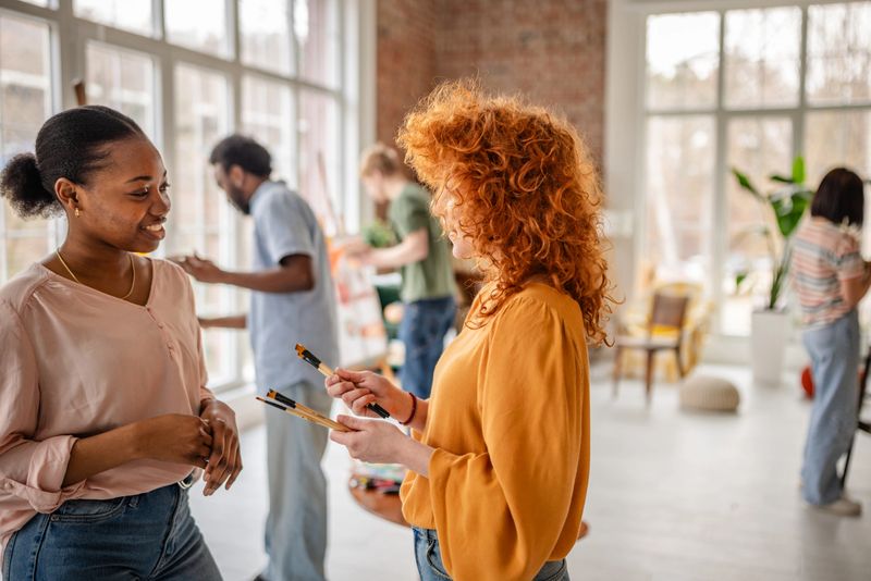In a bright art studio, a diverse group of young artists engages in a creative workshop, sharing ideas and techniques while happily collaborating on their art projects.
