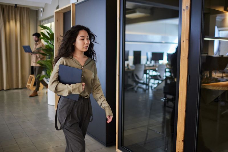 One Millennial office worker walking with a laptop under their arm.