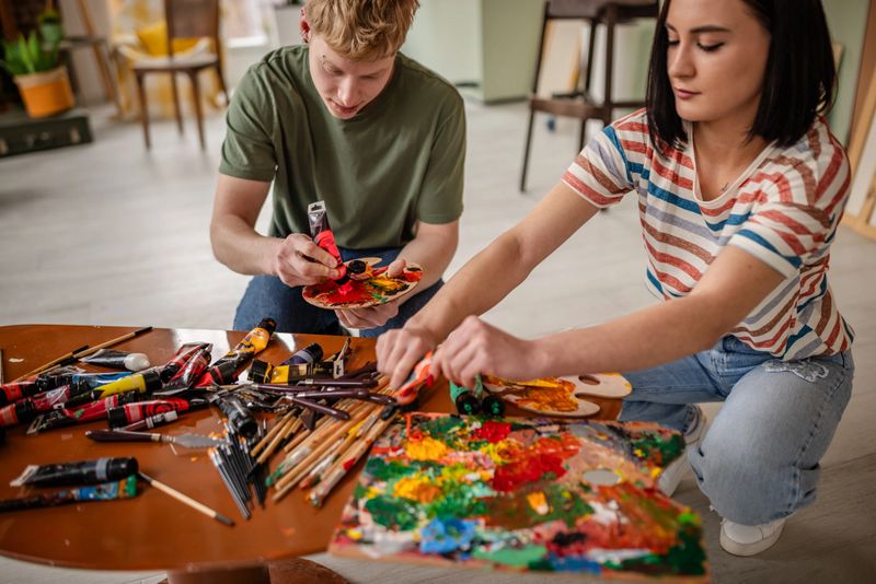 In an art studio, a diverse group of young artists engage in painting, experimenting with colors, and enjoying their creative hobbies. They express joy and inspiration in their craft.