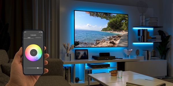 Smartphone controlling blue LED lights behind a TV in a modern living room.