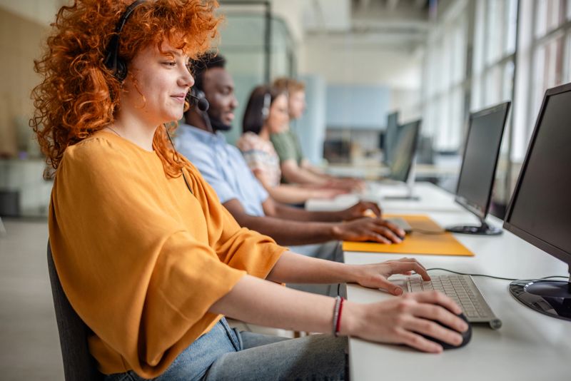 Young adults from diverse backgrounds work together in a call center, providing assistance and advice to clients while using technology to communicate effectively.