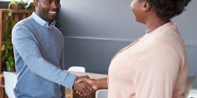 Two people shaking hands in a friendly office setting.