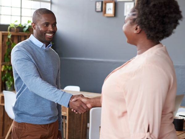 Two people shaking hands in a friendly office setting.