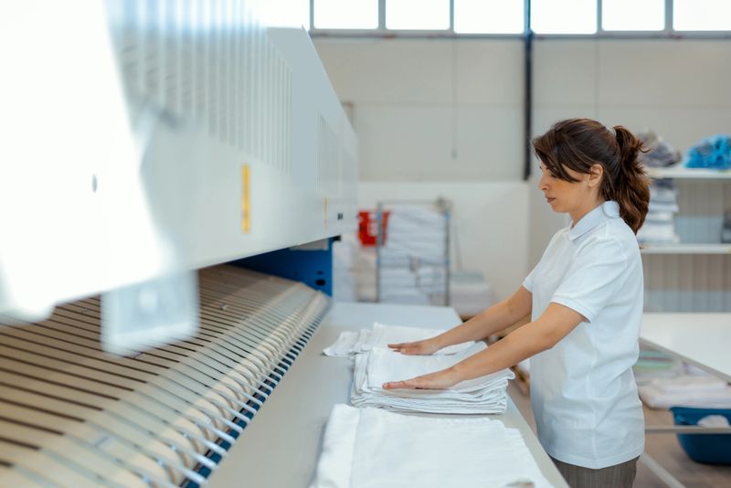 Woman working diligently in her laundry service, folding clothes and managing operations in a small, well-organized shop.