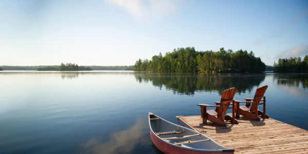 Canoe docked by wooden pier with chairs on a calm lake.