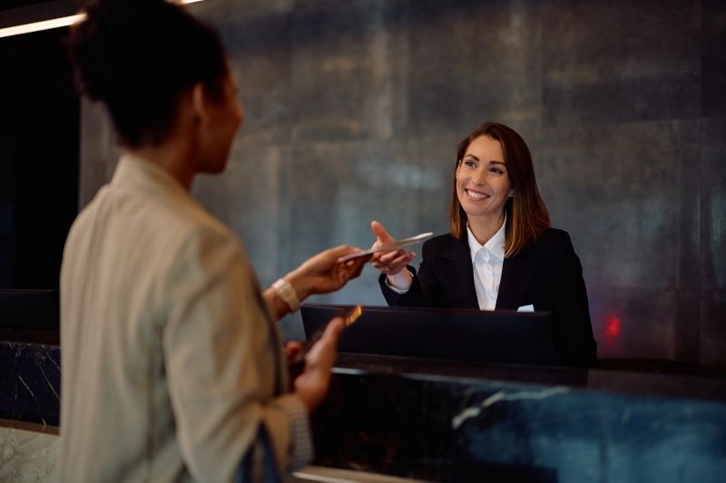 Happy female receptionist serving a female guest at hotel front desk.