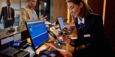 Hotel receptionist assisting a guest at the front desk with a smile.
