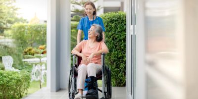 A caregiver pushing an elderly woman in a wheelchair.