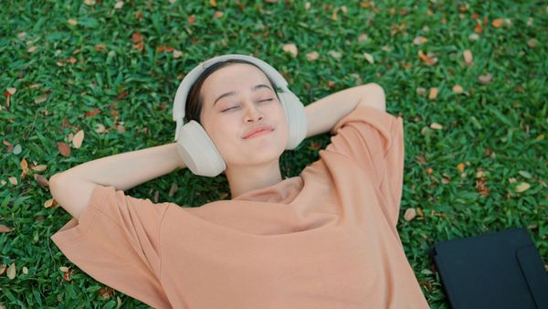 Woman wearing headphones, relaxing on grass with eyes closed.
