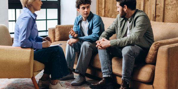 Teen boy talking with adults on couch in a therapy session.