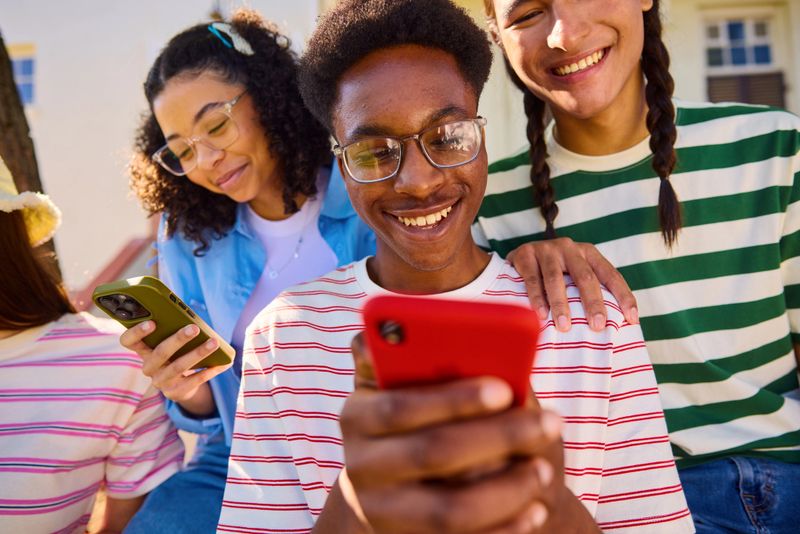 Group of Gen Z teenagers using smartphones together outdoors