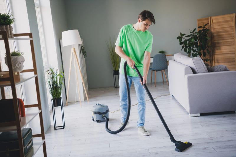 A young man vacuuming in a bright home interior. The minimalist design with greenery accents adds a homely atmosphere.