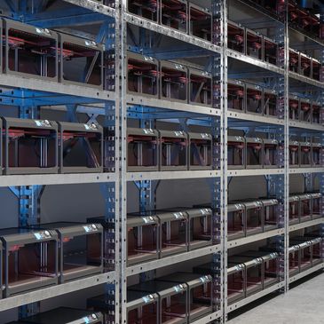 Rows of 3D printers neatly arranged on metal shelves in a spacious industrial room.