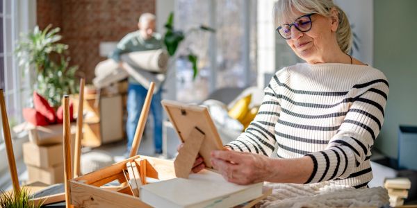 Senior woman holding a framed photo while packing boxes.