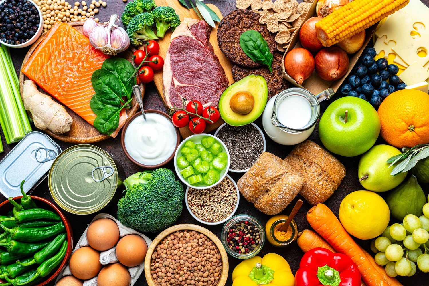 A colorful assortment of fresh fruits, vegetables, meats, and dairy on a dark surface.