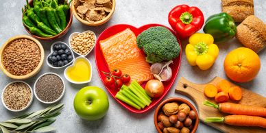 Healthy foods arranged around a heart-shaped plate with salmon and vegetables.