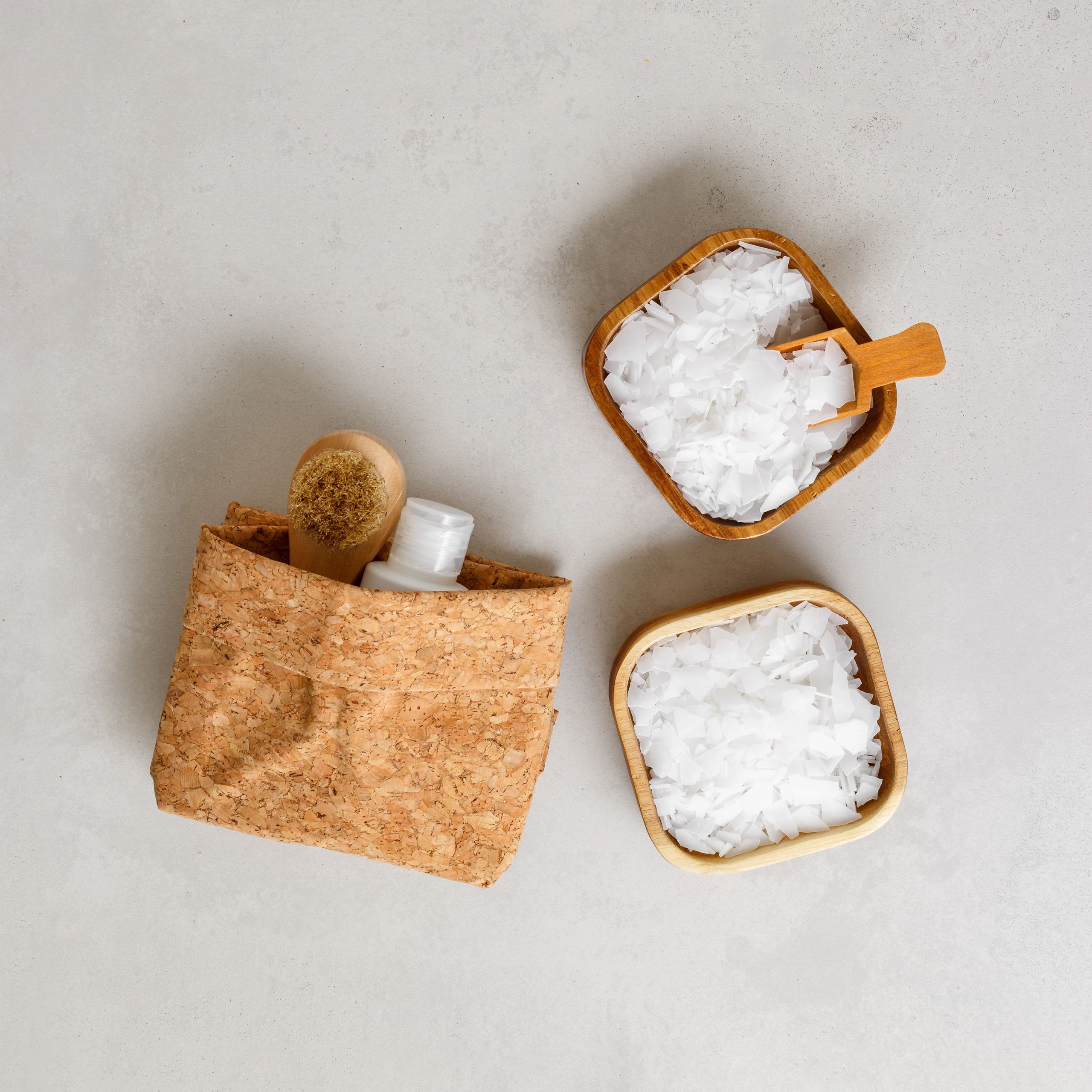 Wooden bowls with white flakes and natural spa items on a light surface.