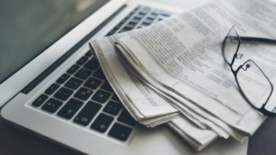 Glasses and newspaper on a laptop keyboard.