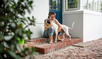 Woman hugging a dog on brick steps outside a house.