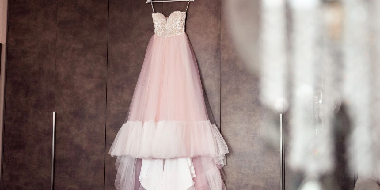 Elegant pink and white strapless gown hanging on a dark wardrobe.