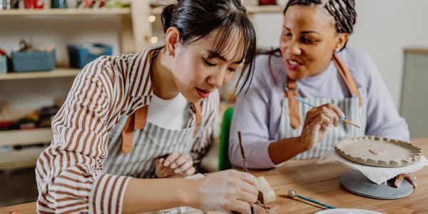 Two women focused on painting pottery together in a cozy studio.