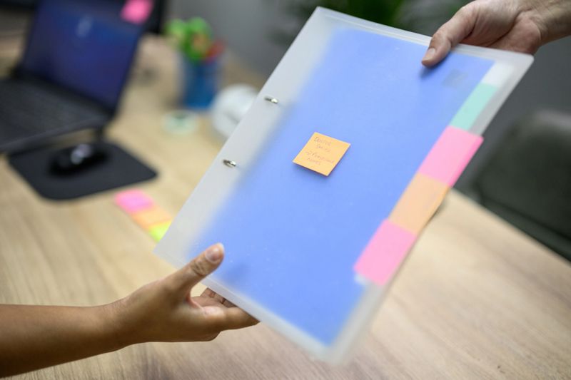 Hospital administrator writing on sticky notes and using laminator in office