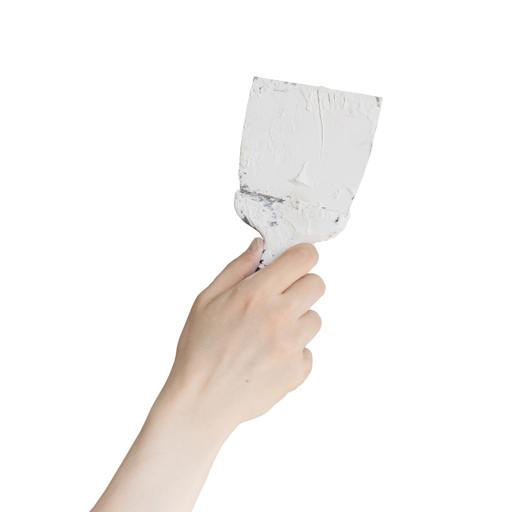 Hand holding a paint scraper covered in white paint.