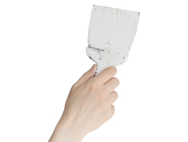 Hand holding a putty knife with white plaster.