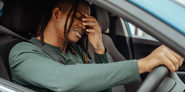 Man in car holding his face, appearing stressed or tired.