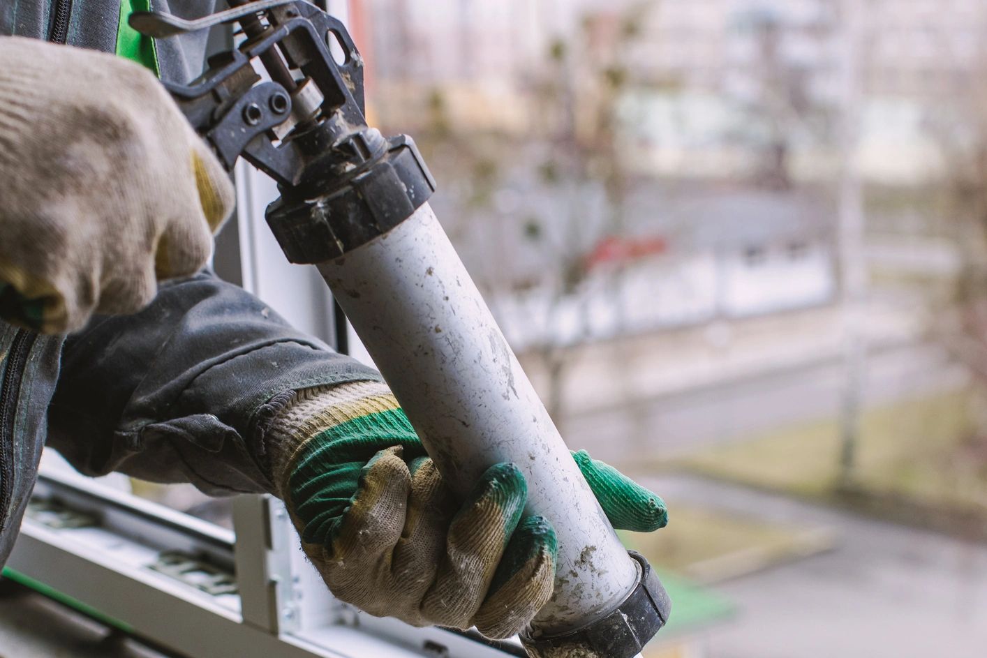 Worker applying sealant to a window frame with a caulking gun.