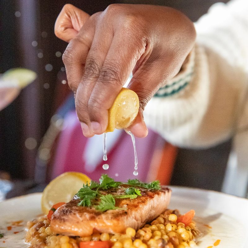 Lemon wedge being squeezed over grilled fresh salmon