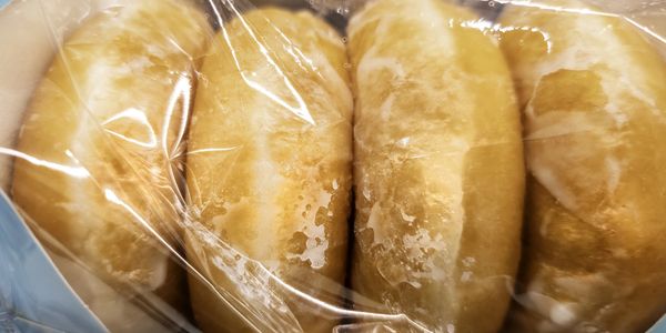 Fresh golden-brown bread rolls wrapped in plastic.