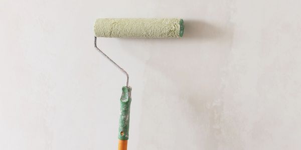 A paint roller with light green paint on a wall.