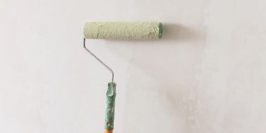 A paint roller against a lightly painted white wall.