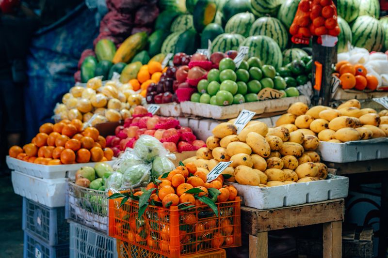 A vibrant display of fresh assorted fruits, including mangoes, apples, and oranges, arranged on a market stall.