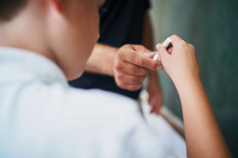 Teacher passing a piece of chalk to a student, preparing for writing on the blackboard in a vibrant classroom setting, fostering an engaging learning environment