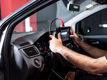 Person using a diagnostic tool on a car's steering wheel.
