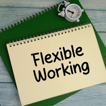 Notebook with 'Flexible Working' text, glasses, plant, and clock on a wooden table.