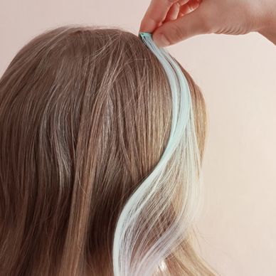 Hand holding a pastel blue hair extension against brown hair.