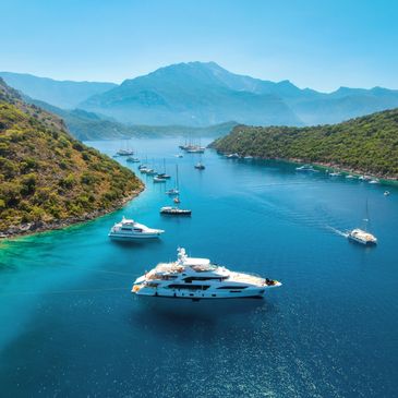 Yachts anchored in a calm bay surrounded by green hills and mountains.